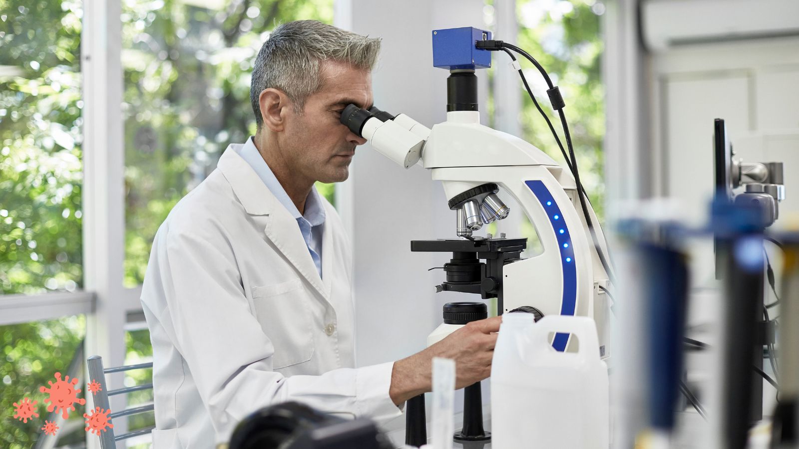 A man in a white lab coat looking through a microscope.